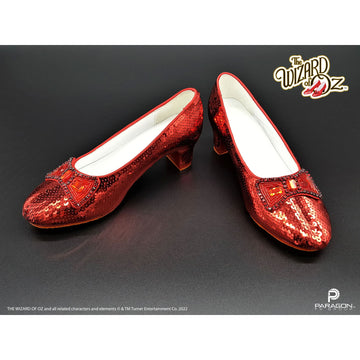 Red sequined shoes with white soles on a dark background, featuring 'The Wizard of Oz' logo. Movie Prop Authentic Replica Dorothy's Ruby Slippers from The Wizard of Oz